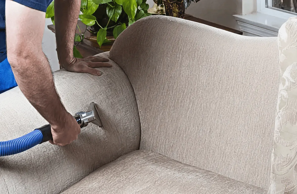 Professional upholstery cleaner deep-cleaning a fabric sofa with a handheld extraction tool and hose, Miami, FL.